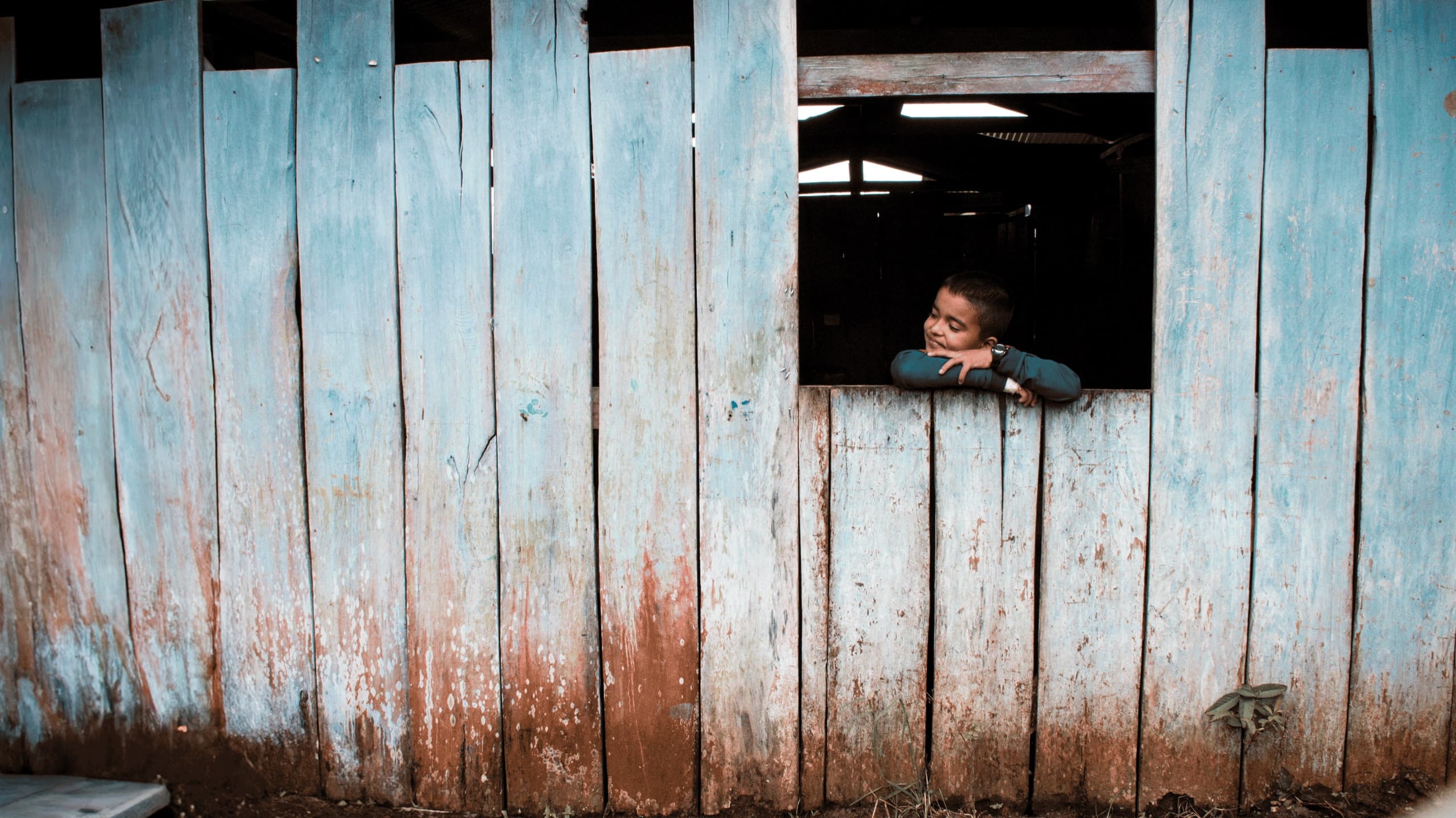 Niño mirando desde la ventana de una vivienda de madera en Caquetá